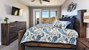 Un dormitorio con cama, ventilador de techo, televisión, cómoda y vistas al exterior.
