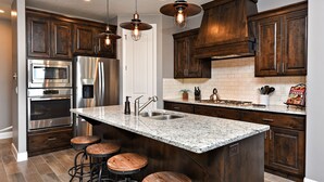 Una cocina moderna con armarios de madera oscura, electrodomésticos de acero inoxidable, encimera de granito y taburetes de bar.