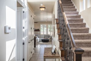 Staircase leads to an upper level, with a bench and framed picture in the foreground.