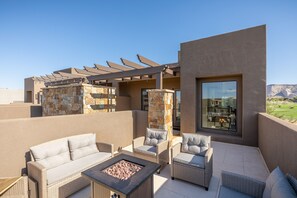 Relax in style with a sofa, armchairs, and fire pit on this outdoor patio, surrounded by a pergola and offering a view of the golf course and distant mountains.