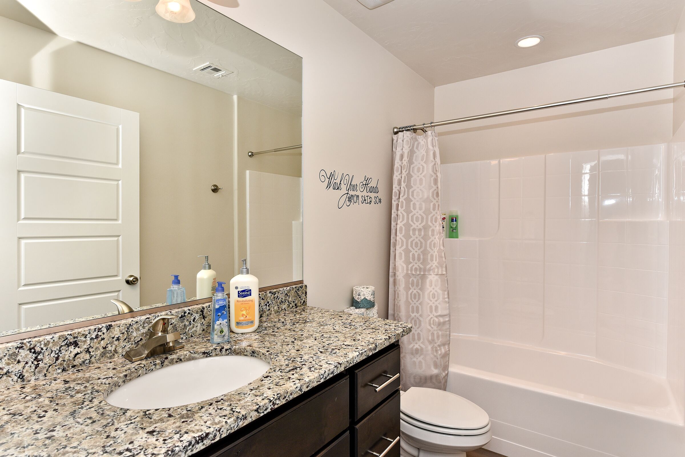 A bathroom with a granite countertop, a white sink, a mirror, a toilet, and a shower with a curtain.