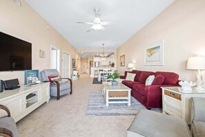 A spacious living room with a red sofa, a white coffee table, a ceiling fan, and a TV.