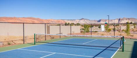 A tennis court with a chain-link fence, a net, and a clear blue sky.