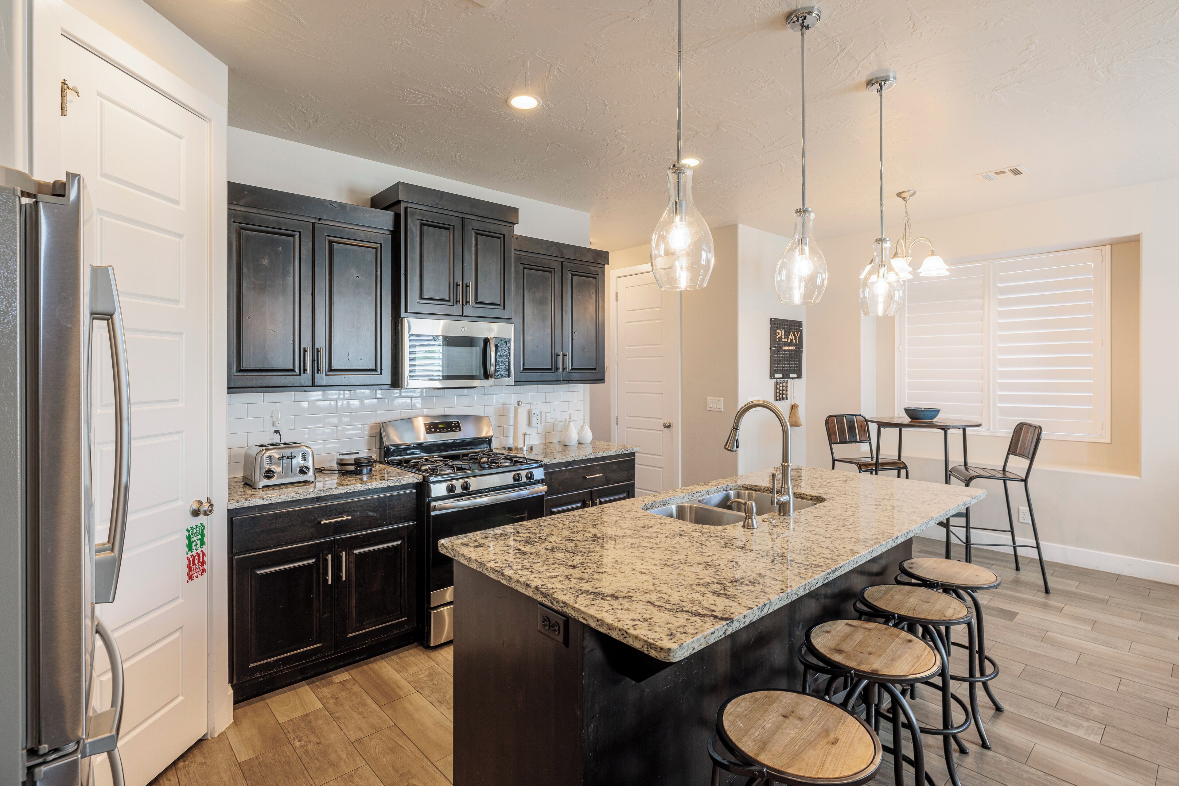 A modern kitchen with dark cabinets, stainless steel appliances, a granite countertop, and a bar area with stools.