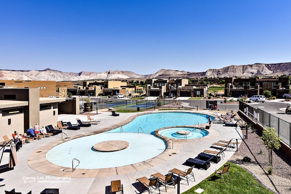 Un espace piscine comprenant plusieurs piscines, des chaises longues et offrant une vue sur les montagnes en arrière-plan.