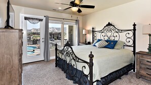 A bedroom with a bed, a ceiling fan, a nightstand, and a view of a swimming pool through a glass door.