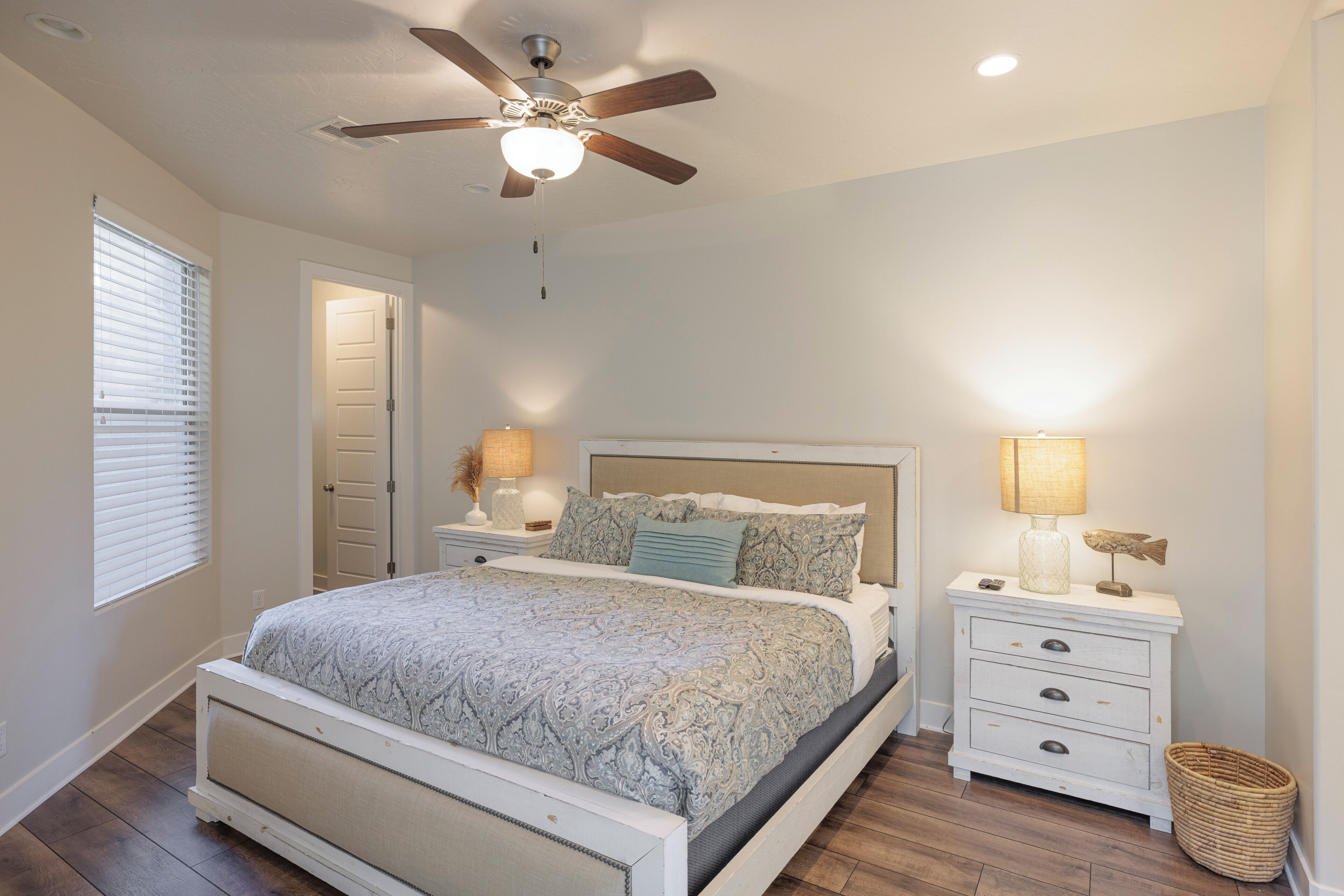 A bedroom with a bed, nightstands, a ceiling fan, and a window with blinds.