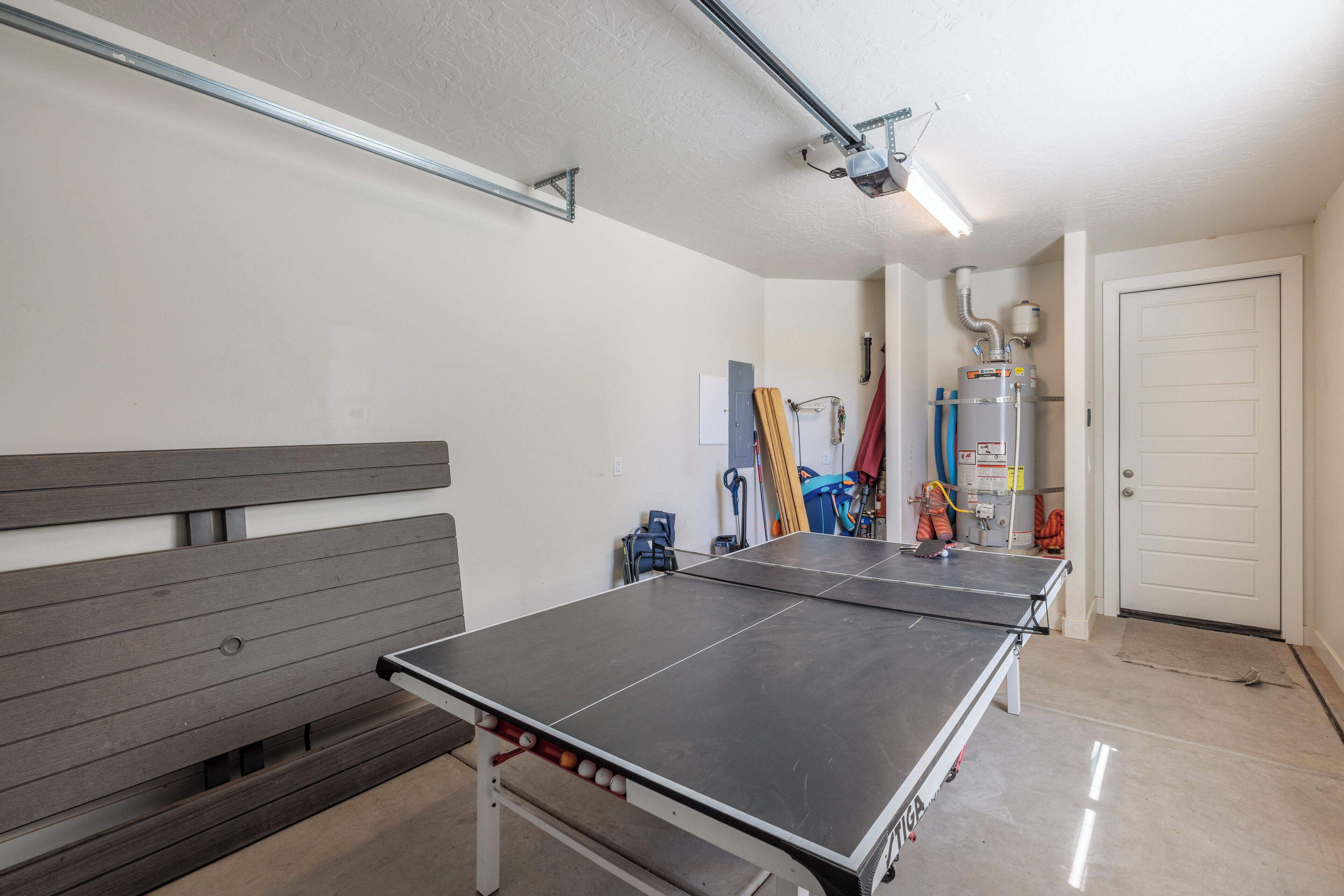 Una mesa de ping pong en una habitación con un banco, una puerta y un calentador de agua.