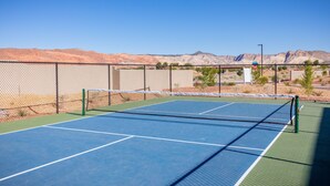 En tennisbana med ett stängsel av sammanlänkade metallkedjor, ett nät och en klarblå himmel.