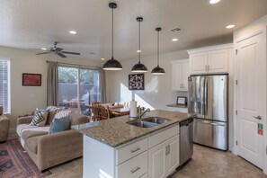 A modern kitchen with a built-in island, stainless steel appliances, pendant lighting, and a dining area with a view.