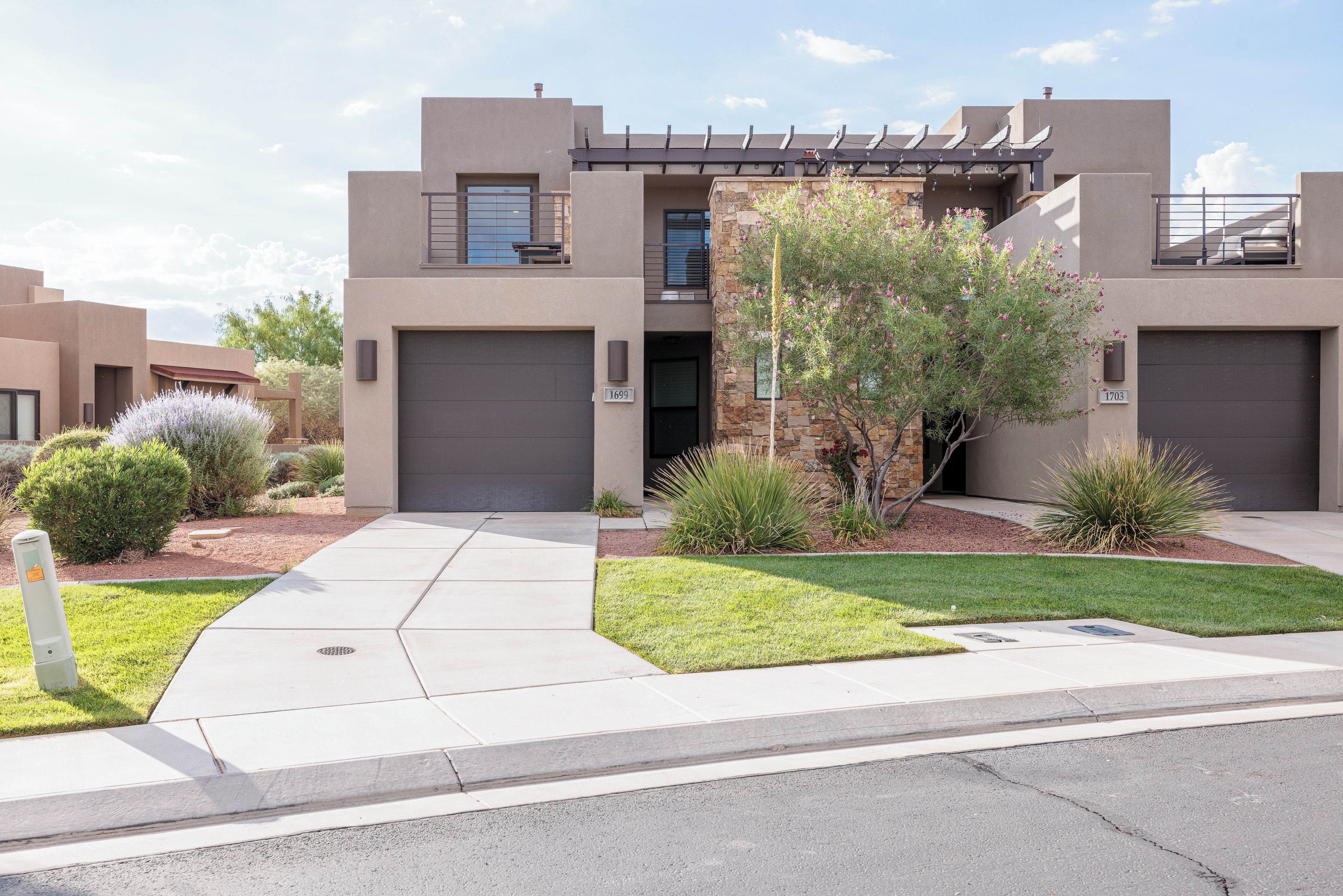 A modern two-story residential building with a garage, a well-maintained lawn, and a variety of landscaping.