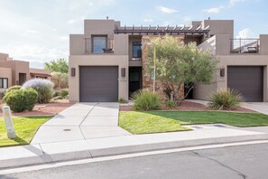 A modern two-story residential building with a garage, a well-maintained lawn, and a variety of landscaping.