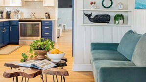 A modern kitchen with blue cabinets, a stainless steel range hood, and a dining area with a wooden table and chairs.