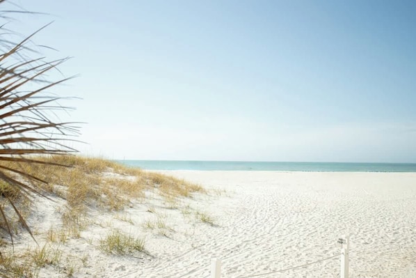 A beach with sand, a clear sky, and a sign.