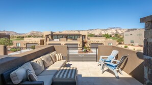 A rooftop patio with a sofa and chairs, a view of a mountainous landscape, and a building in the background. - Sweeping Red Rock Views - 4BR close to Pool & Hot Tub (St. George)