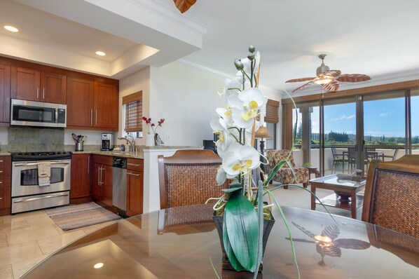 A modern kitchen with wooden cabinets, stainless steel appliances, and a dining area with a glass table and wicker chairs.