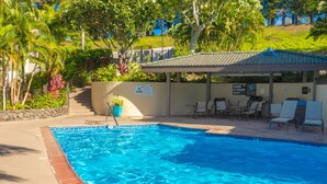 Una piscina con borde de baldosas, rodeada de sillas de descanso y una zona de estar cubierta.