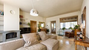 Een ruime woonkamer met een beige modulaire bank, een open haard, een televisie en een houten salontafel met wijnglazen.