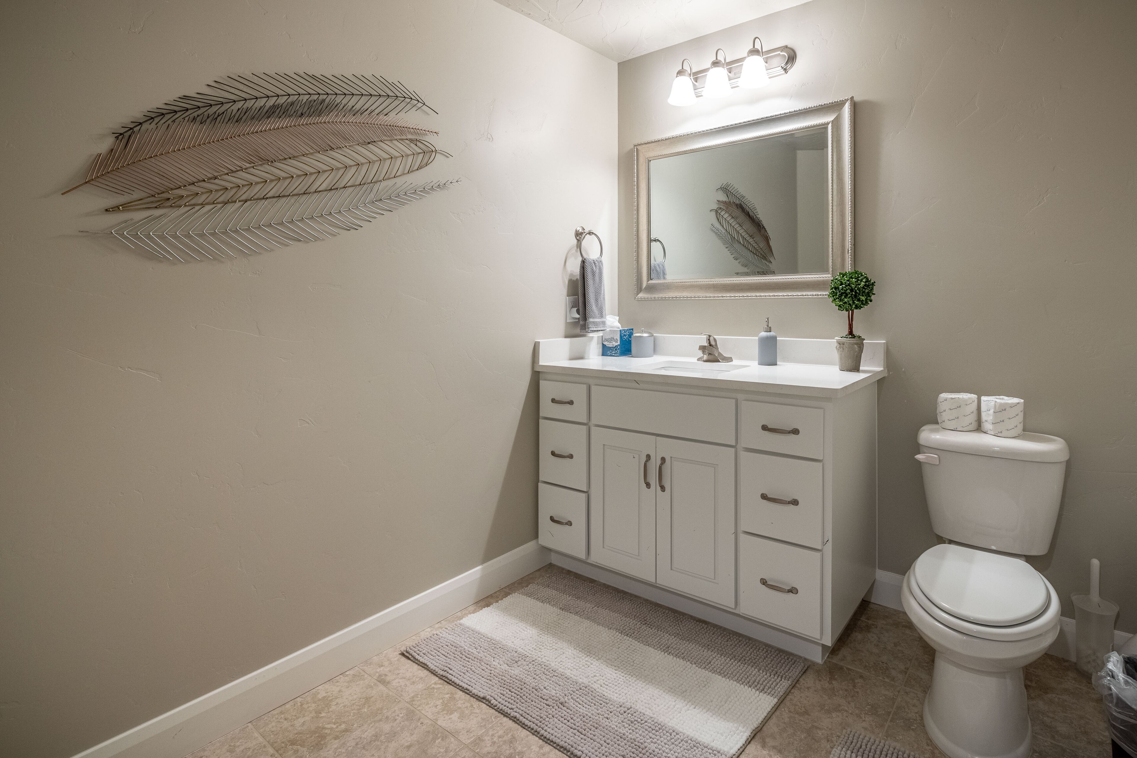 Un bagno con un vanità bianca, uno specchio, un water e un elemento decorativo a forma di foglia sulla parete.