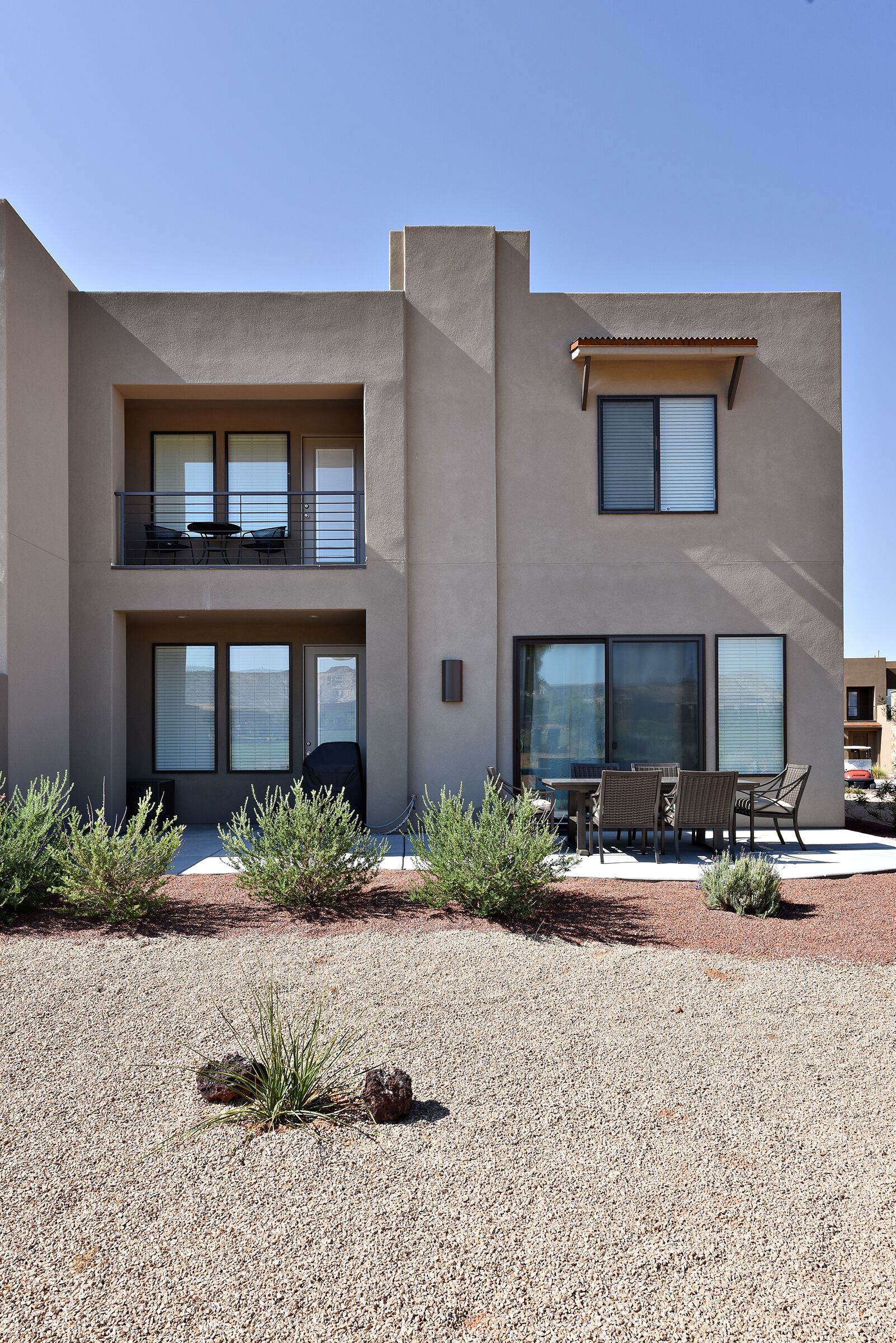 A modern two-story building with a balcony, large windows, and outdoor seating area.