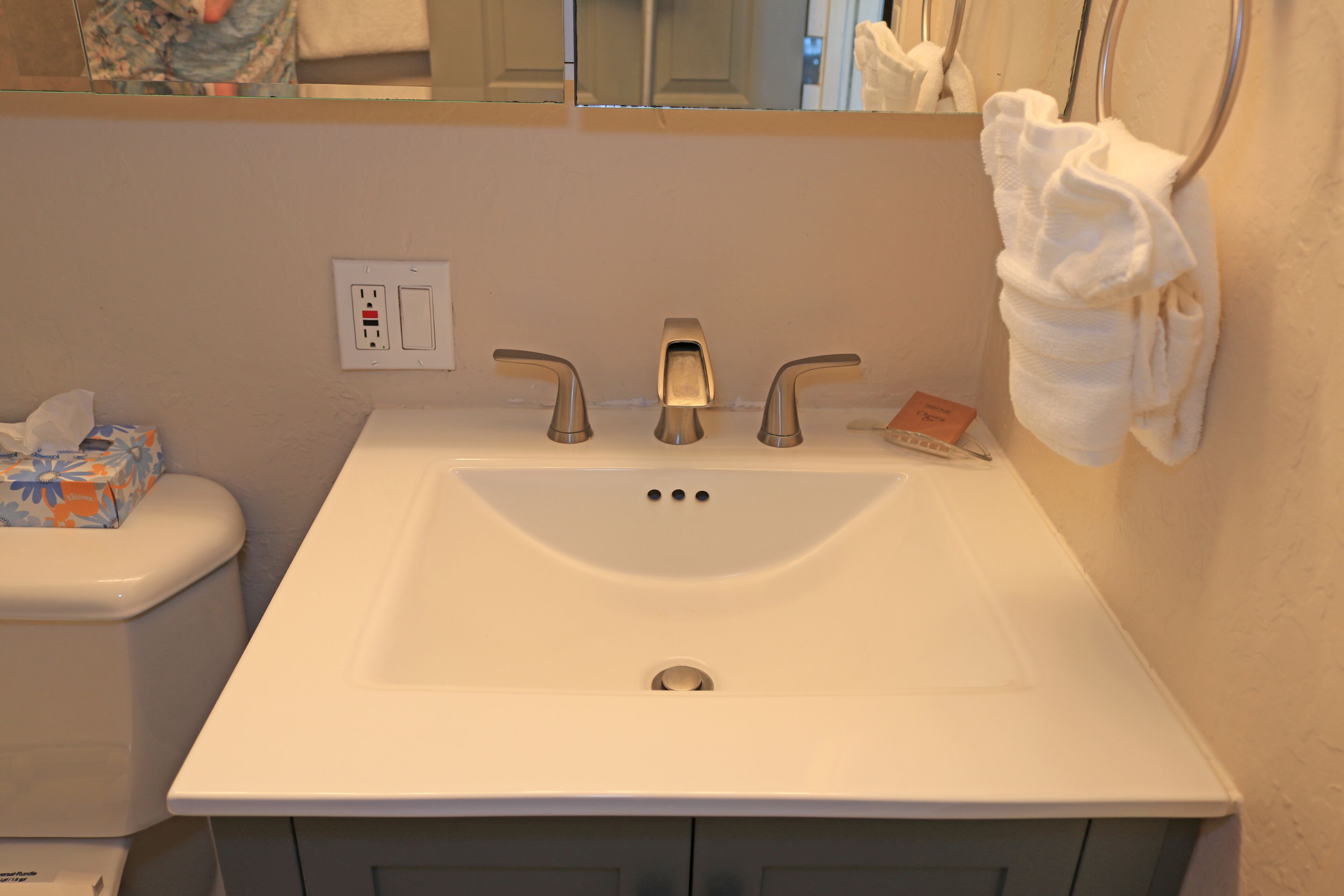 A bathroom with a white sink, two faucets, a mirror, and a towel rack.