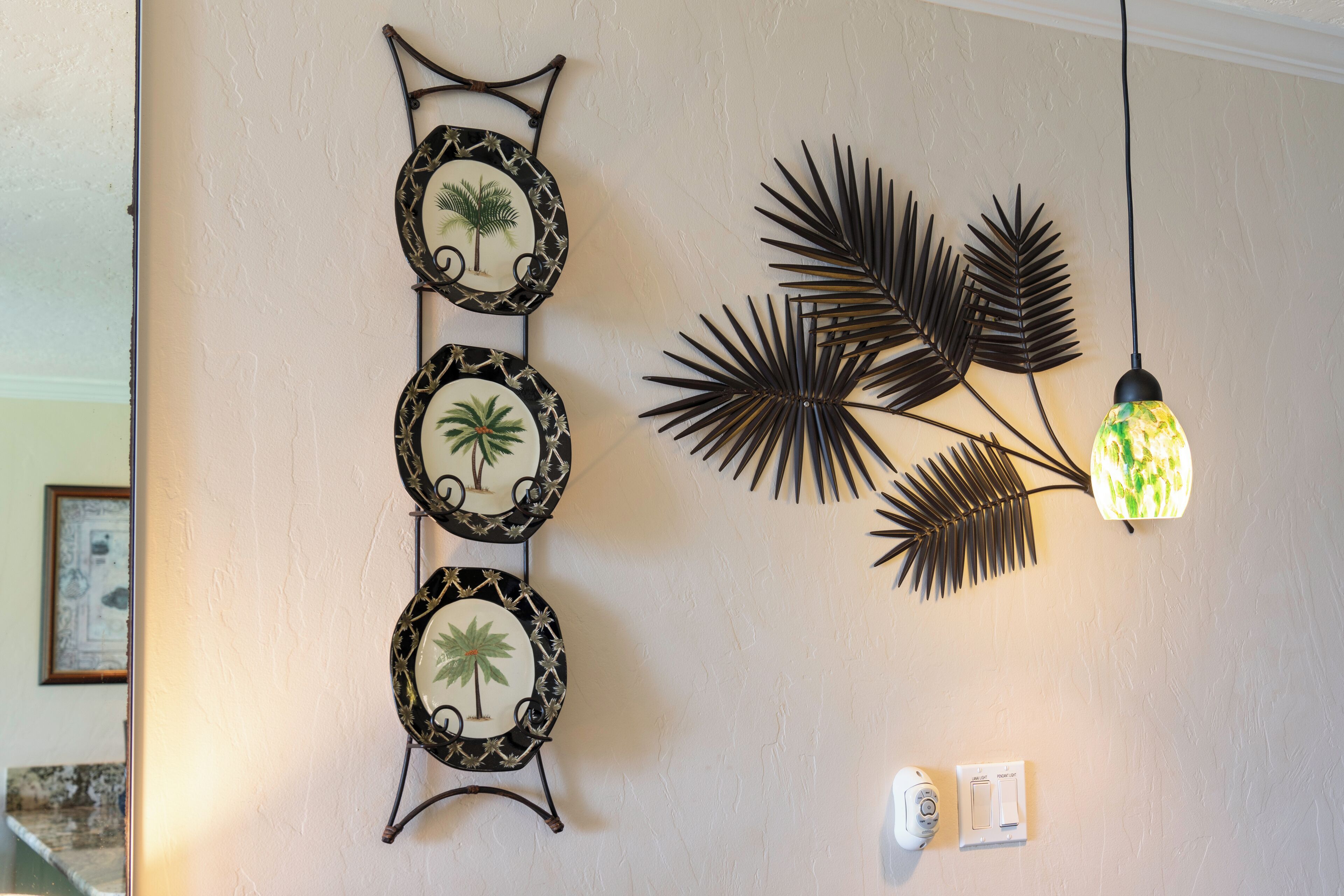 Un mur orné de trois tableaux encadrés représentant des palmiers et d’un luminaire décoratif orné de feuilles de palmier.