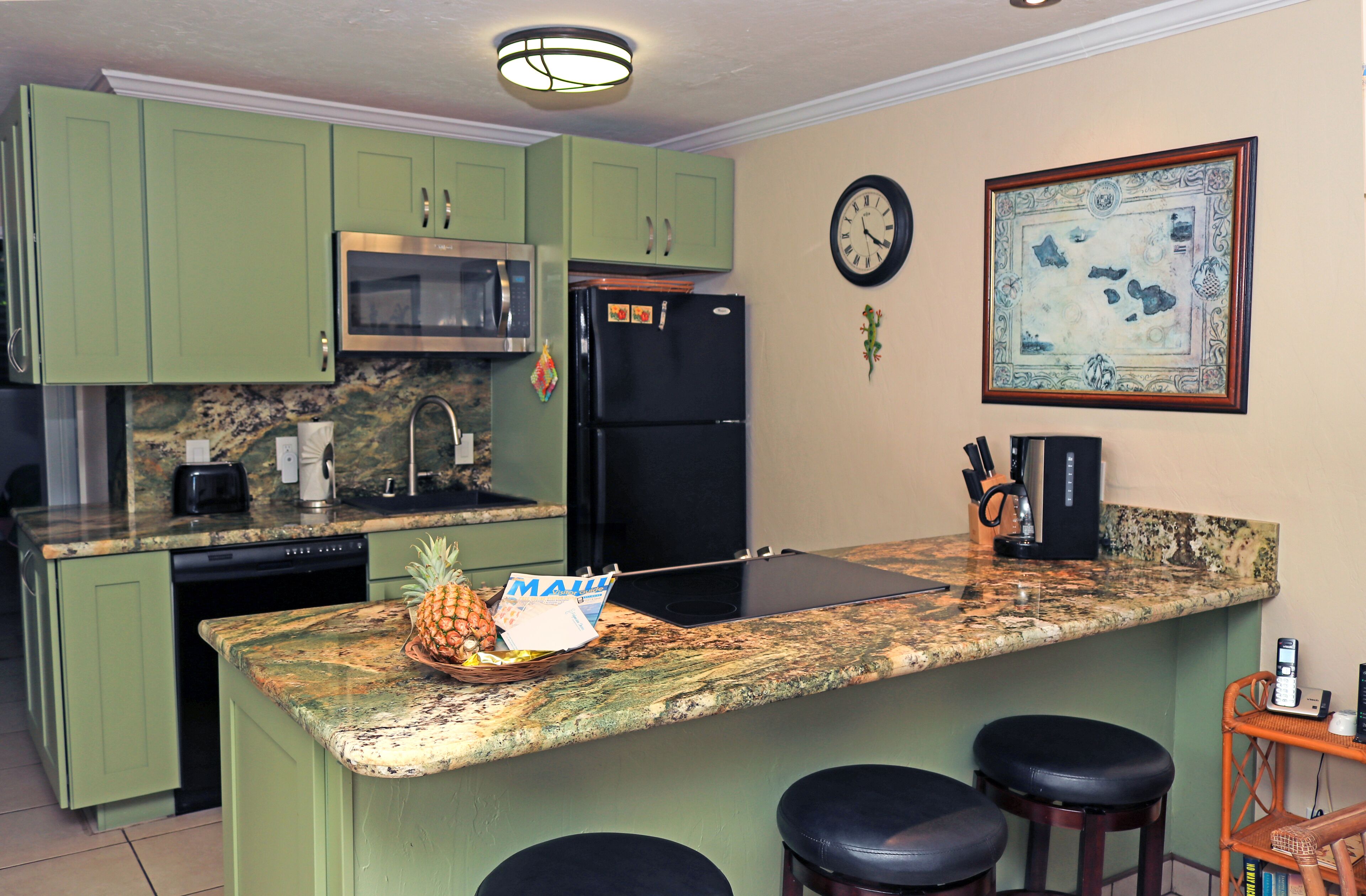 A kitchen with green cabinets, a microwave, a refrigerator, a clock, and a framed picture on the wall.