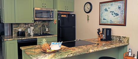 A kitchen with green cabinets, a microwave, a refrigerator, a clock, and a framed picture on the wall.