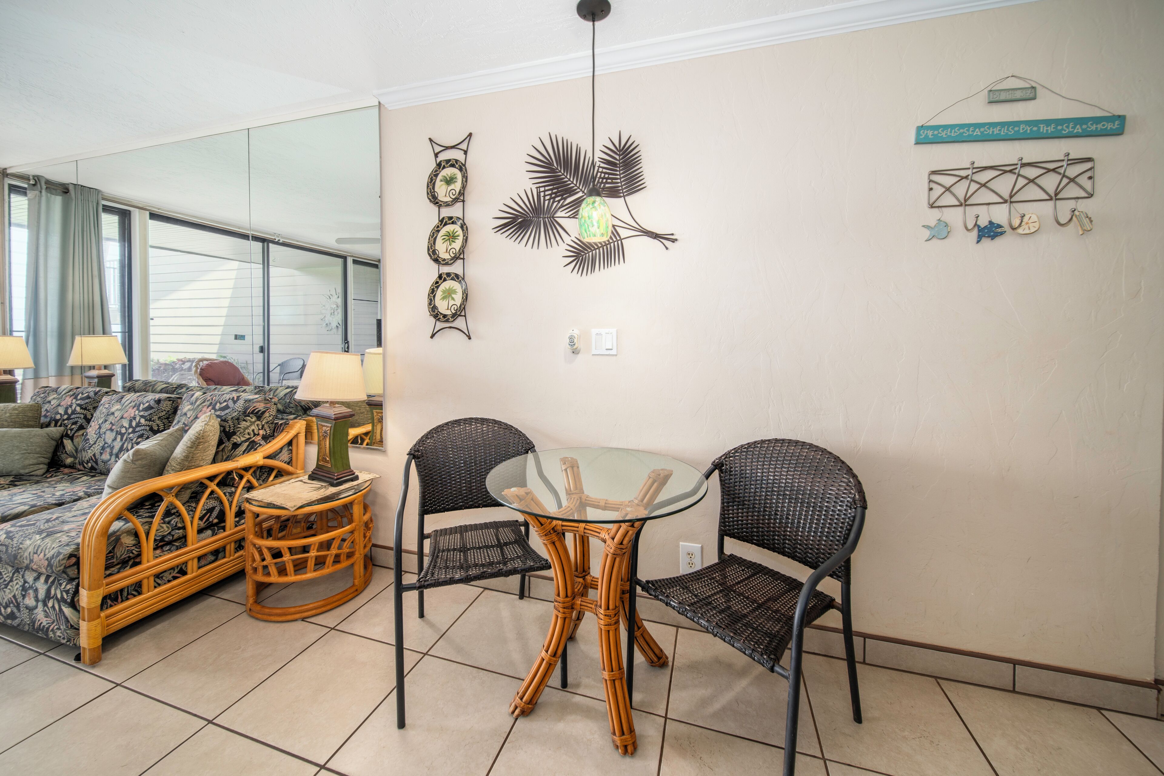 A room with a glass-top table, wicker chairs, a sofa, and a decorative wall piece.