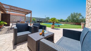 Een terras buiten met wicker meubilair, een zwembad en een stenen muur.