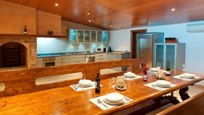 Een eethoek met een houten tafel gedekt voor een maaltijd, een open haard van baksteen en een moderne keuken op de achtergrond.