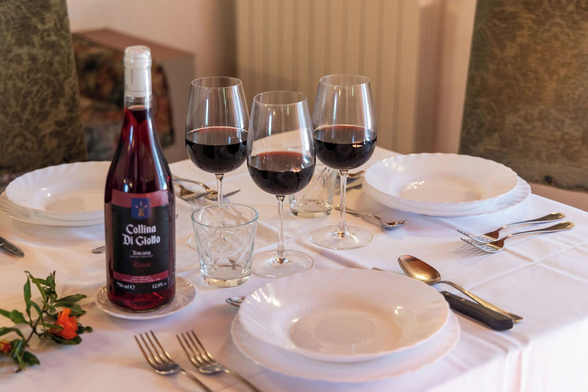 Mesa servida con copas de vino, una botella y vajilla.