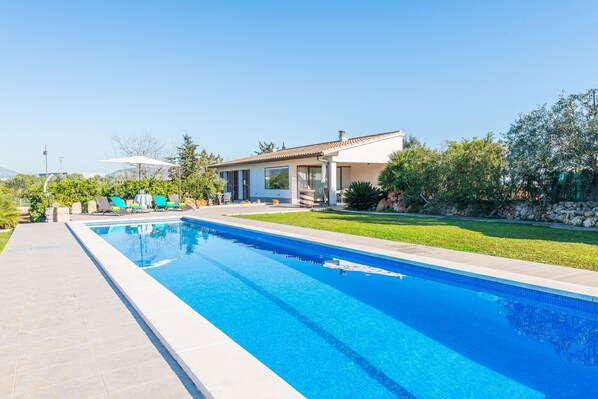 A swimming pool with a clear blue water, surrounded by a paved walkway.