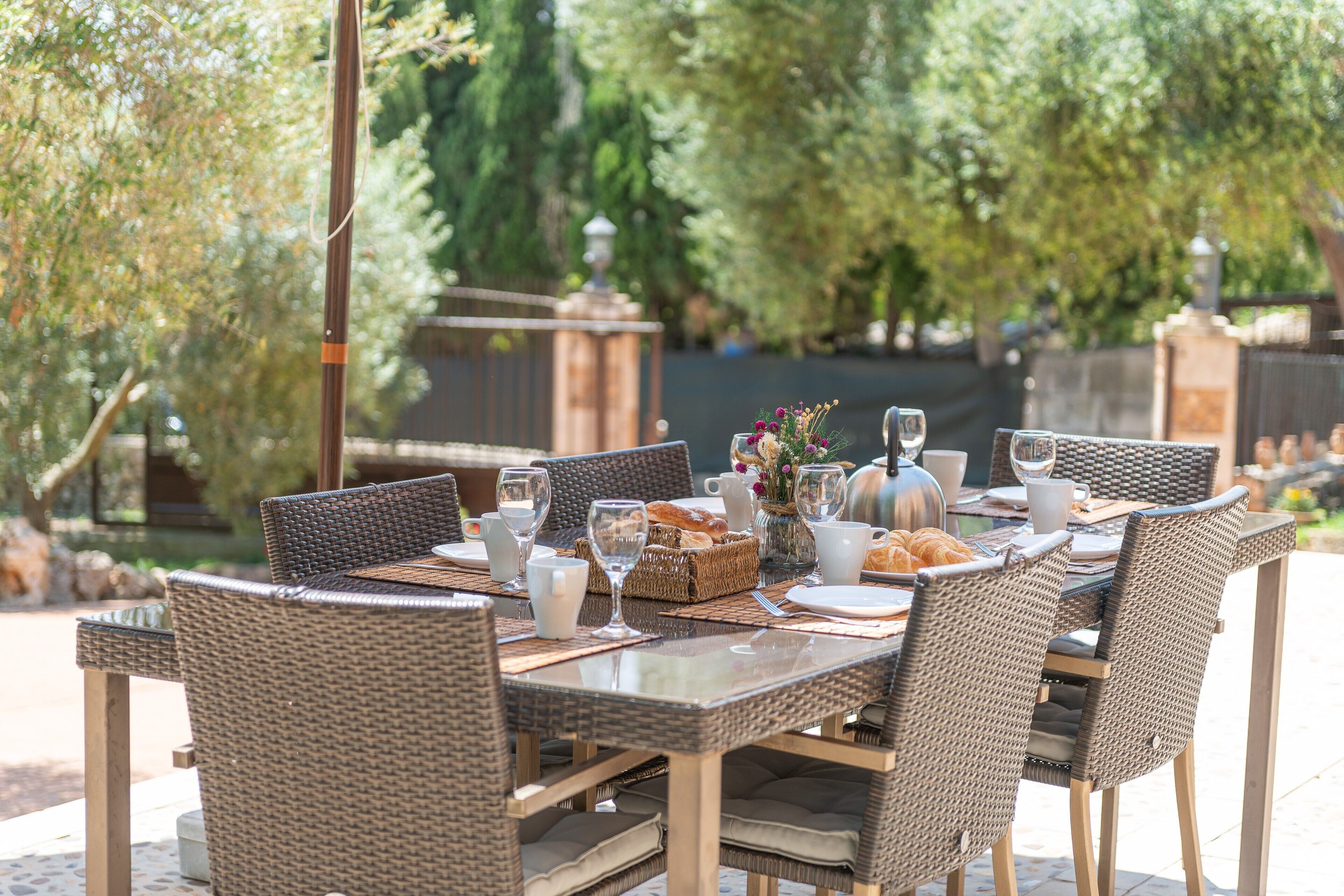 Un espace de restauration en plein air, avec des chaises en osier et une table en verre, entouré de verdure.