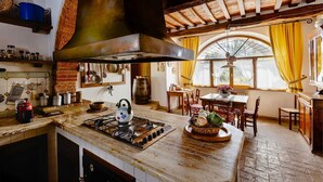 Une cuisine rustique avec un cuisinière à gaz, une grande cheminée et un coin repas comprenant une table et des chaises.