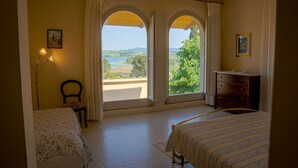 Quarto com cama, penteadeira, cadeira e vista para a paisagem através de janelas em arco.