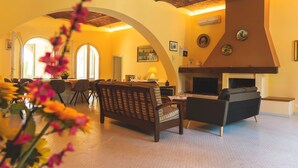 Uma sala de estar ampla com lareira, uma área de refeições com mesa e cadeiras, e um sofá.