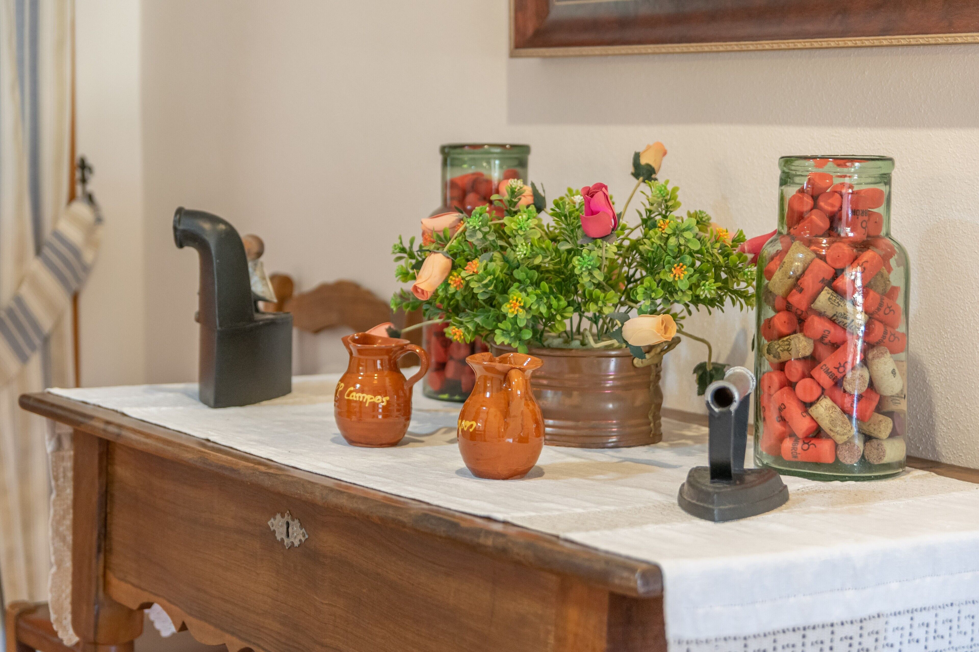 A wooden table with ceramic pitchers, a potted plant, and a jar of corks.