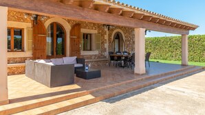 A covered outdoor seating area with a sofa, dining table, and chairs.