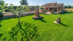 A stone house with a tiled roof, surrounded by a well-maintained lawn and a swimming pool.
