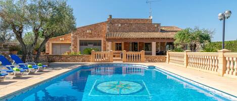 A swimming pool with lounge chairs and a house in the background.