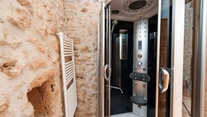 A stone-walled bathroom with a glass-enclosed shower, a white towel rack, and a wooden door.
