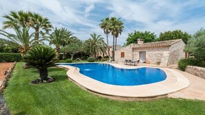 A swimming pool with a stone house and palm trees in the background.
