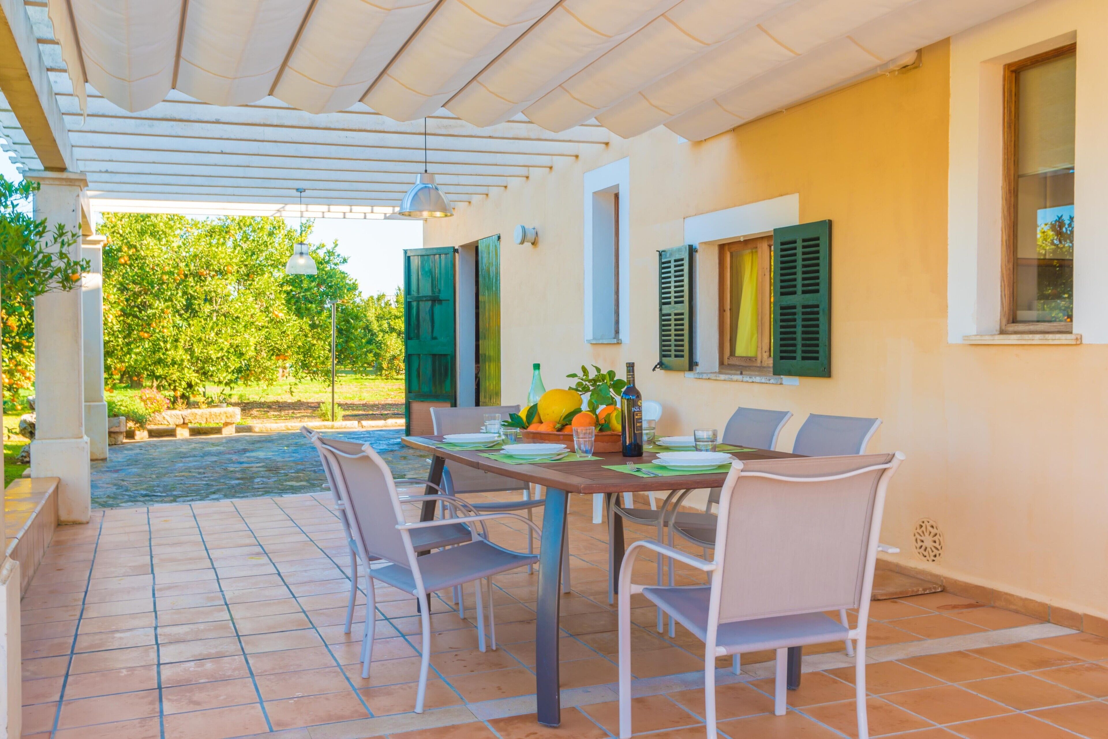 Une terrasse extérieure avec une table dressée pour le repas, entourée de chaises, et une pergola au-dessus.