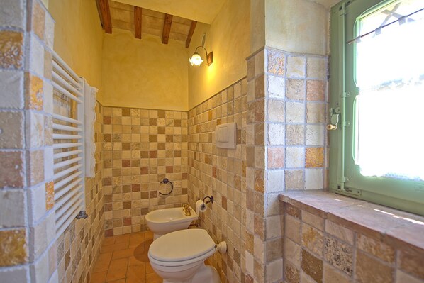 Une salle de bain avec un carrelage au sol, des toilettes, un bidet et une fenêtre dotée d’un cadre vert.