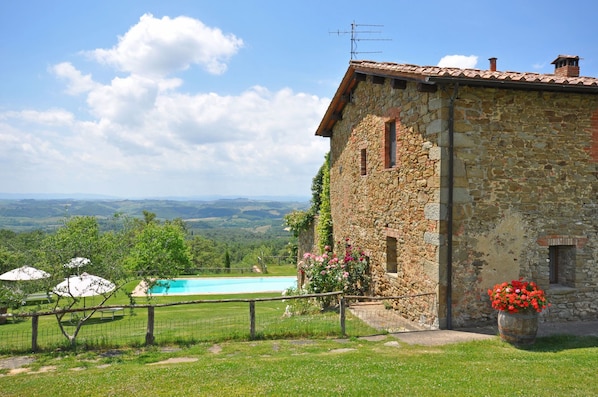 A stone building with a pool, surrounded by a fenced area and a view of the countryside.