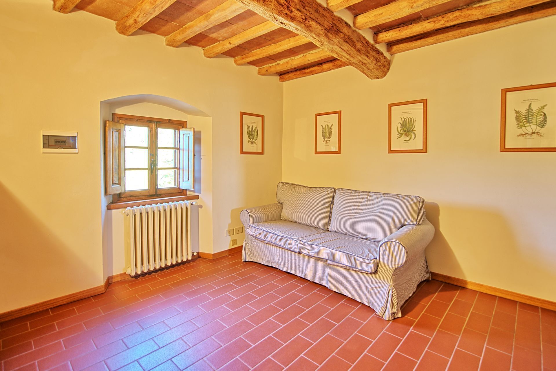 Une pièce chaleureuse avec un plafond en bois, un radiateur, une fenêtre avec des volets et un canapé à rayures.