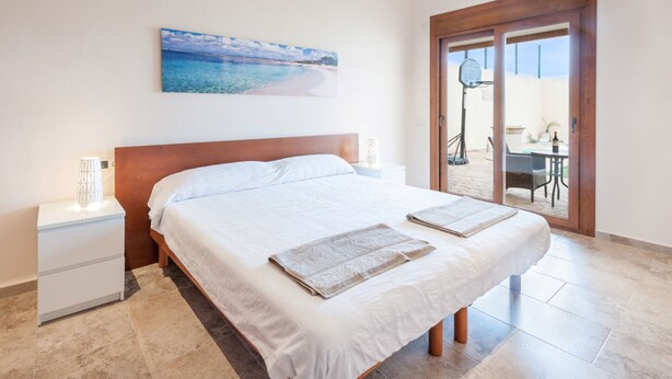 A bedroom with a large bed, a nightstand, a wall-mounted painting, and a sliding glass door leading to a balcony. - CAS PEIX - ADULTS ONLY  - Villa with private pool in Sa Pobla. Free WiFi (Sa Pobla)