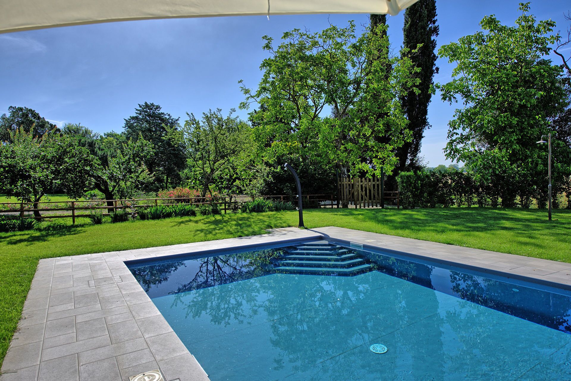 A rectangular swimming pool with a clear blue water surface, surrounded by a paved deck.