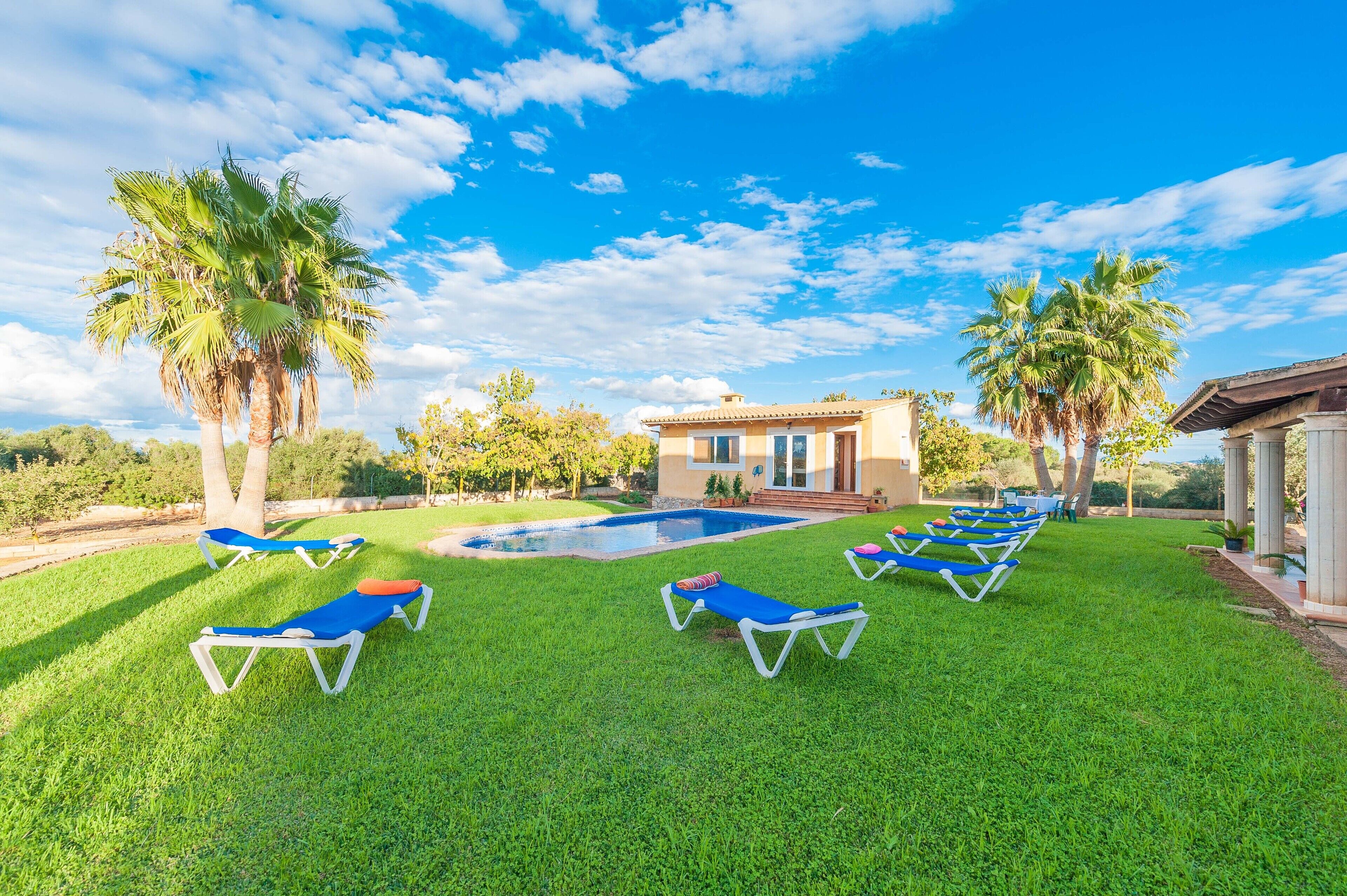 A pool area with lounge chairs, palm trees, and a building with a tiled roof.